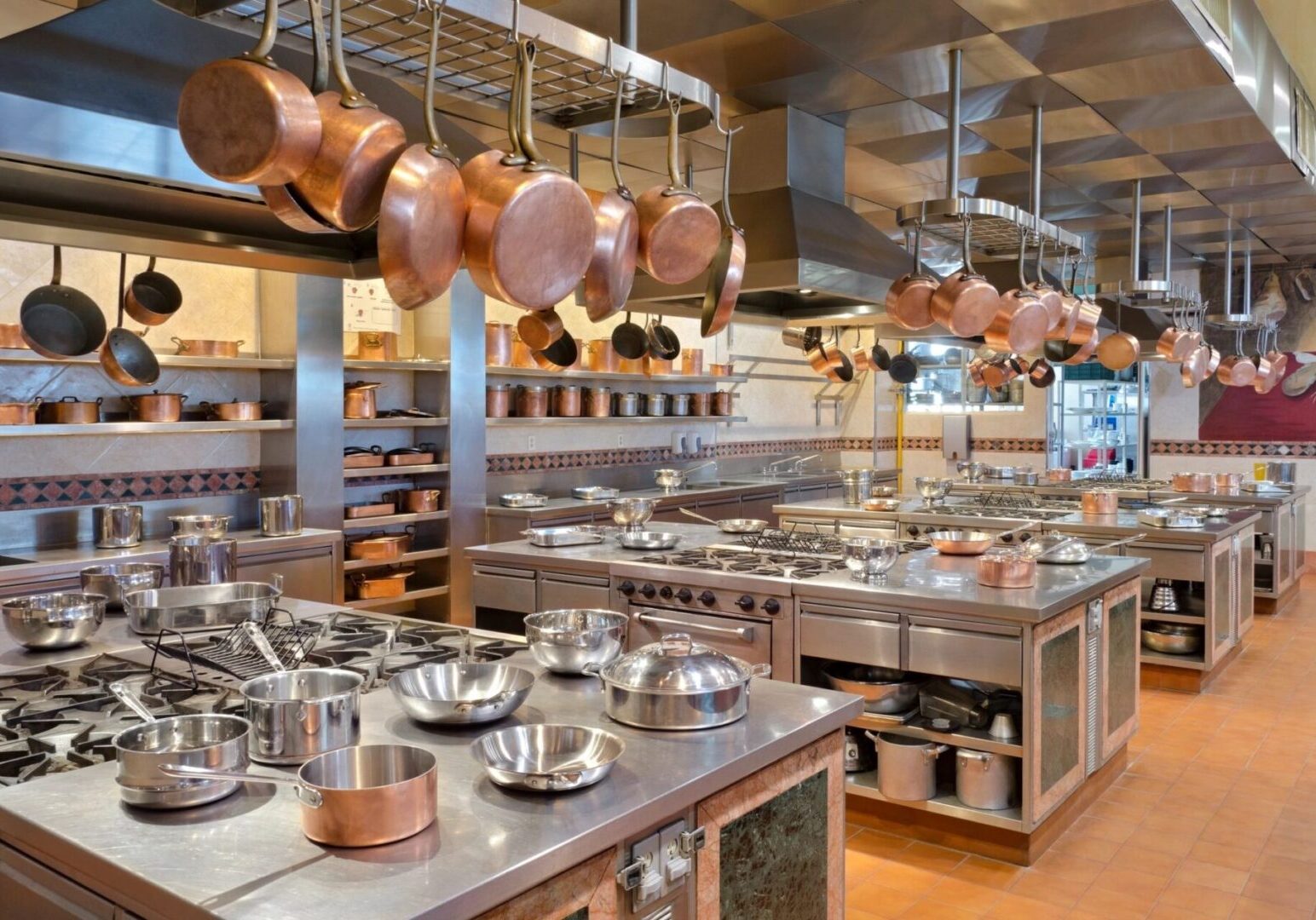 A professional kitchen with hanging copper pots and multiple cooking stations.